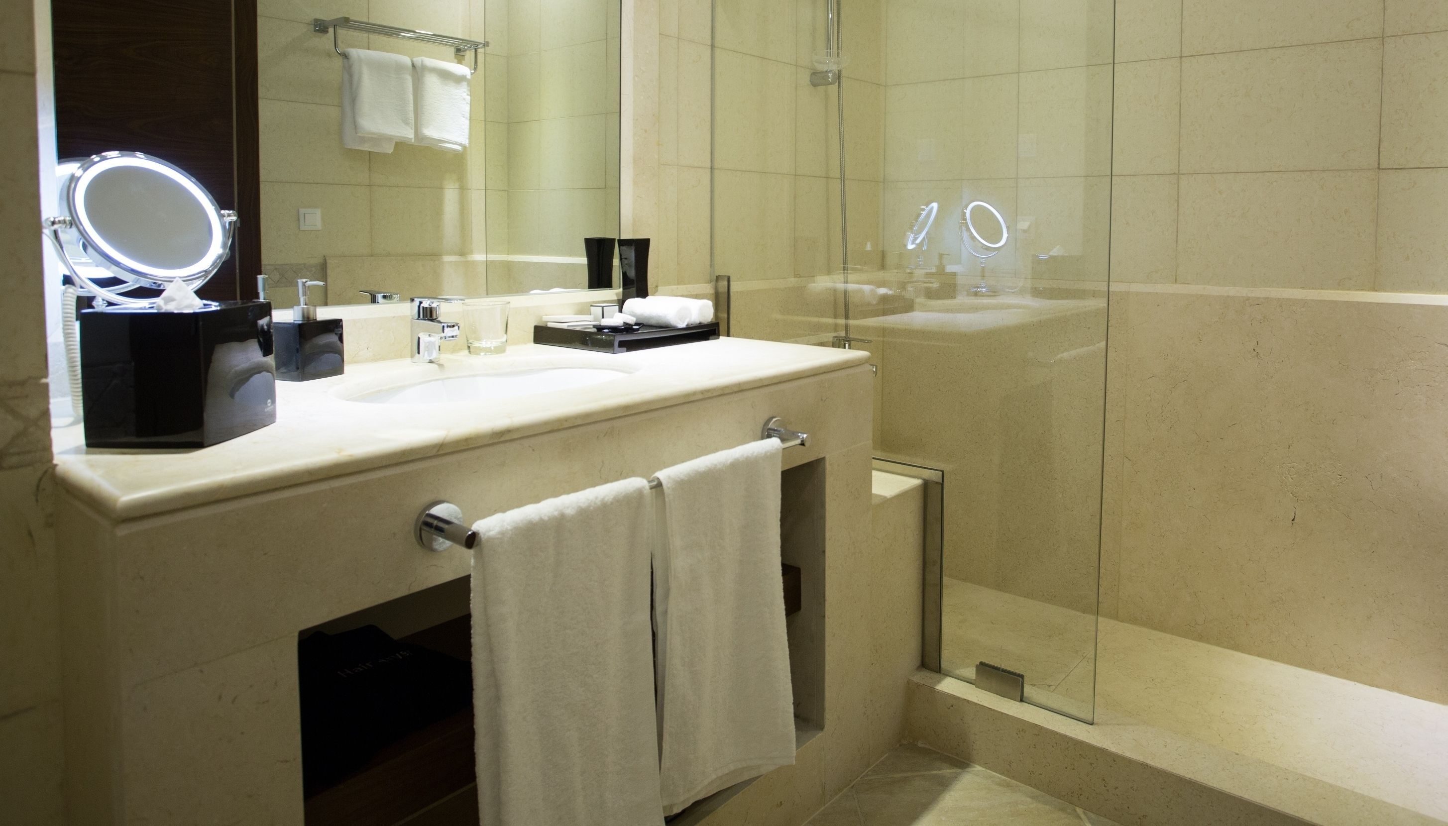 Un bagno moderno con un mobile lavabo, uno specchio illuminato, uno spazio doccia in vetro e un appendi-asciugamani.