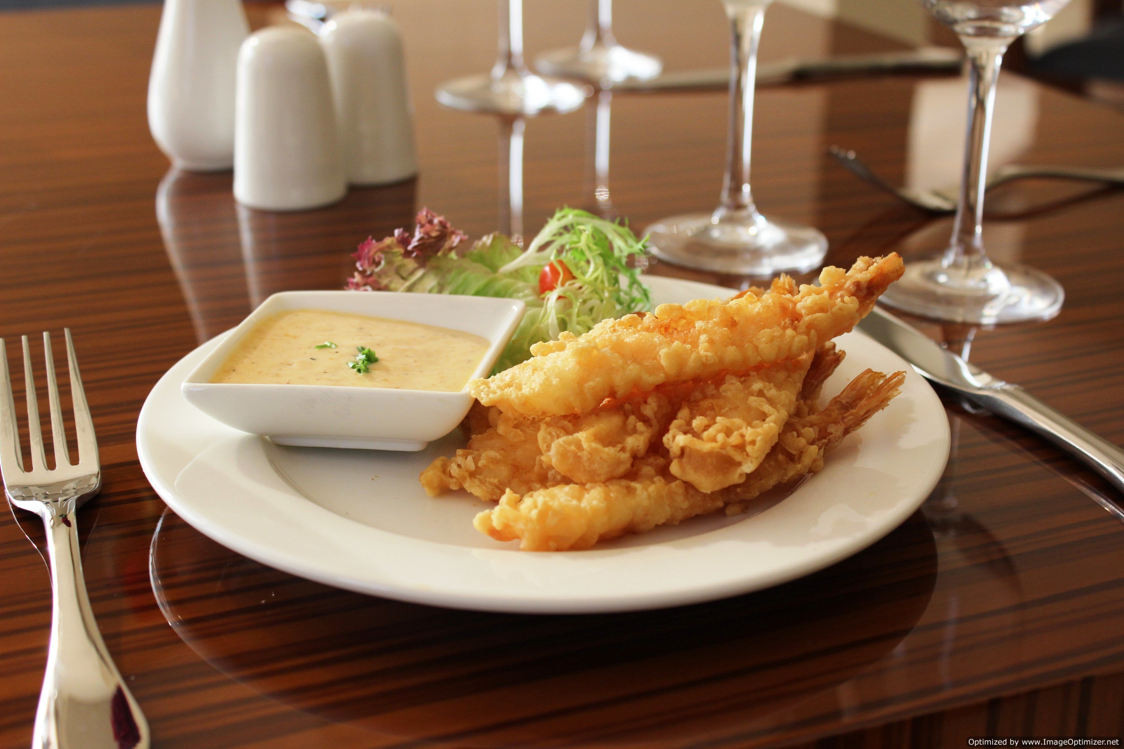 A plate with fried fish, a small bowl of sauce, and a side salad on a wooden table.
