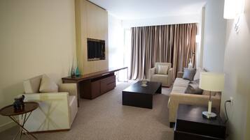 Quarto de hotel moderno com sofá, poltrona, mesa de centro e televisão fixada na parede.