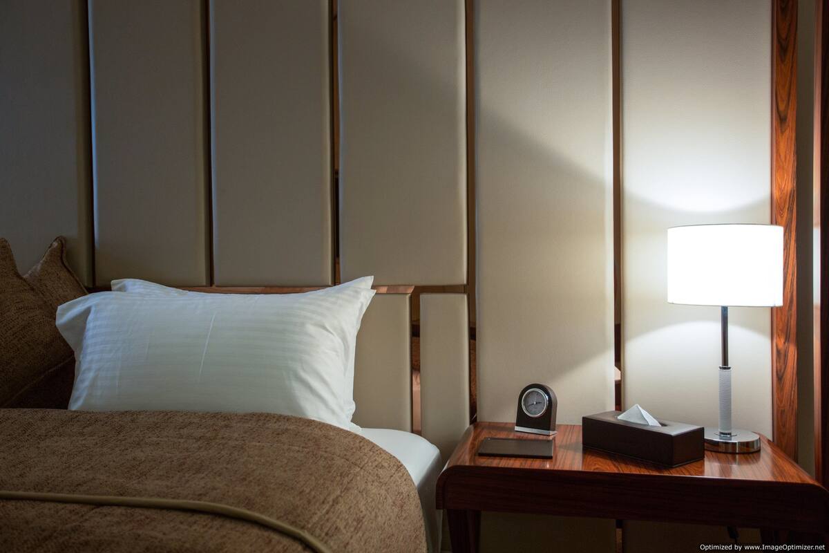 A hotel room with a bed, a nightstand with a lamp, and a clock.