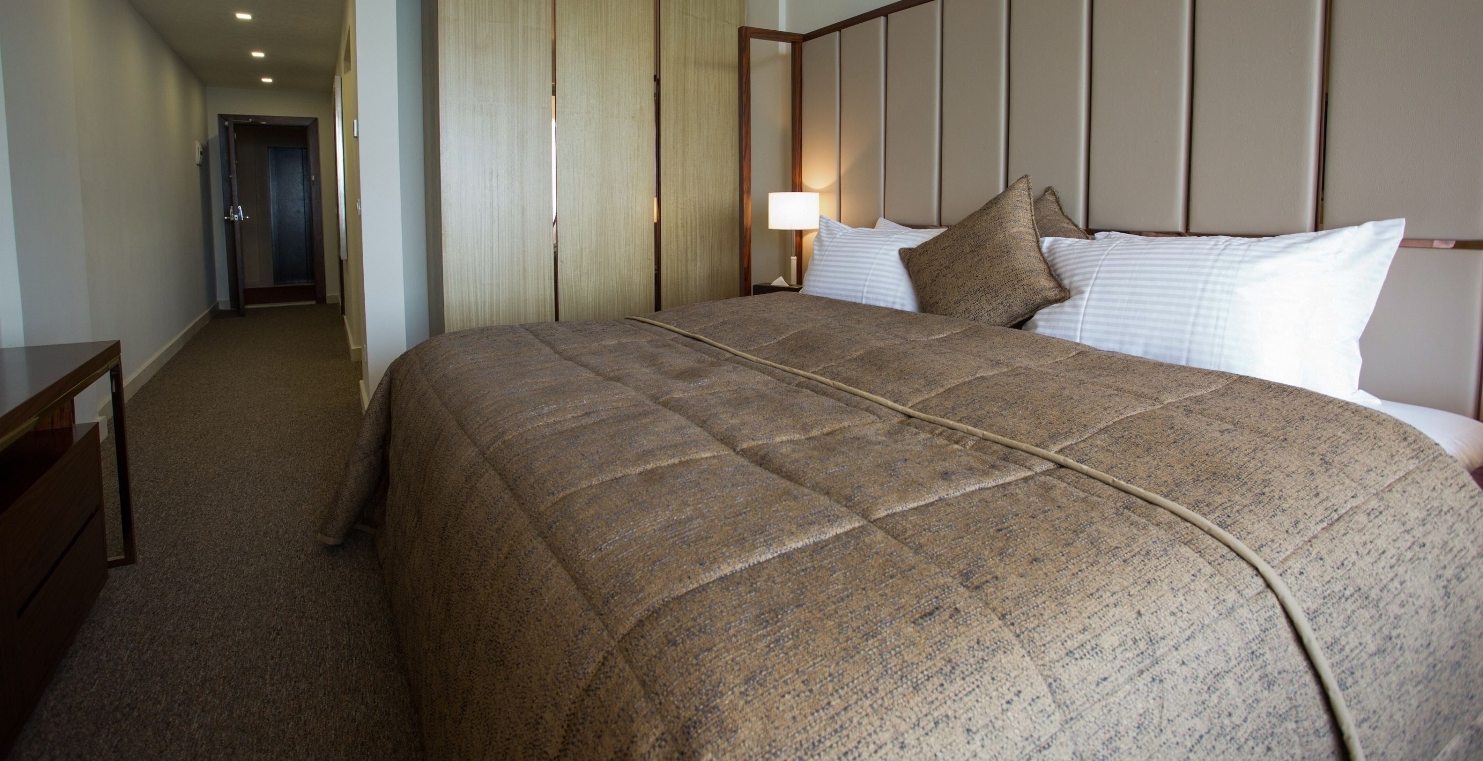 Habitación de hotel con una cama grande, una mesita de noche, una lámpara y una puerta que da a otra habitación.