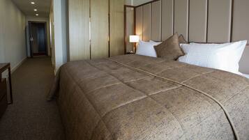 Habitación de hotel con una cama grande, una mesita de noche, una lámpara y una puerta que da a otra habitación.
