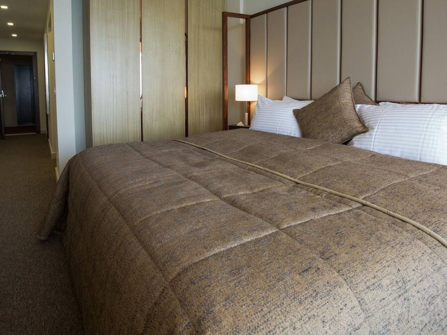 A hotel room with a large bed, a bedside table, a lamp, and a door leading to another room.