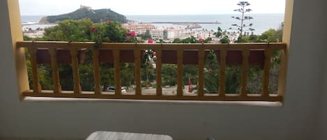 Un balcon avec vue sur la mer et une colline. On y trouve deux chaises et une table.