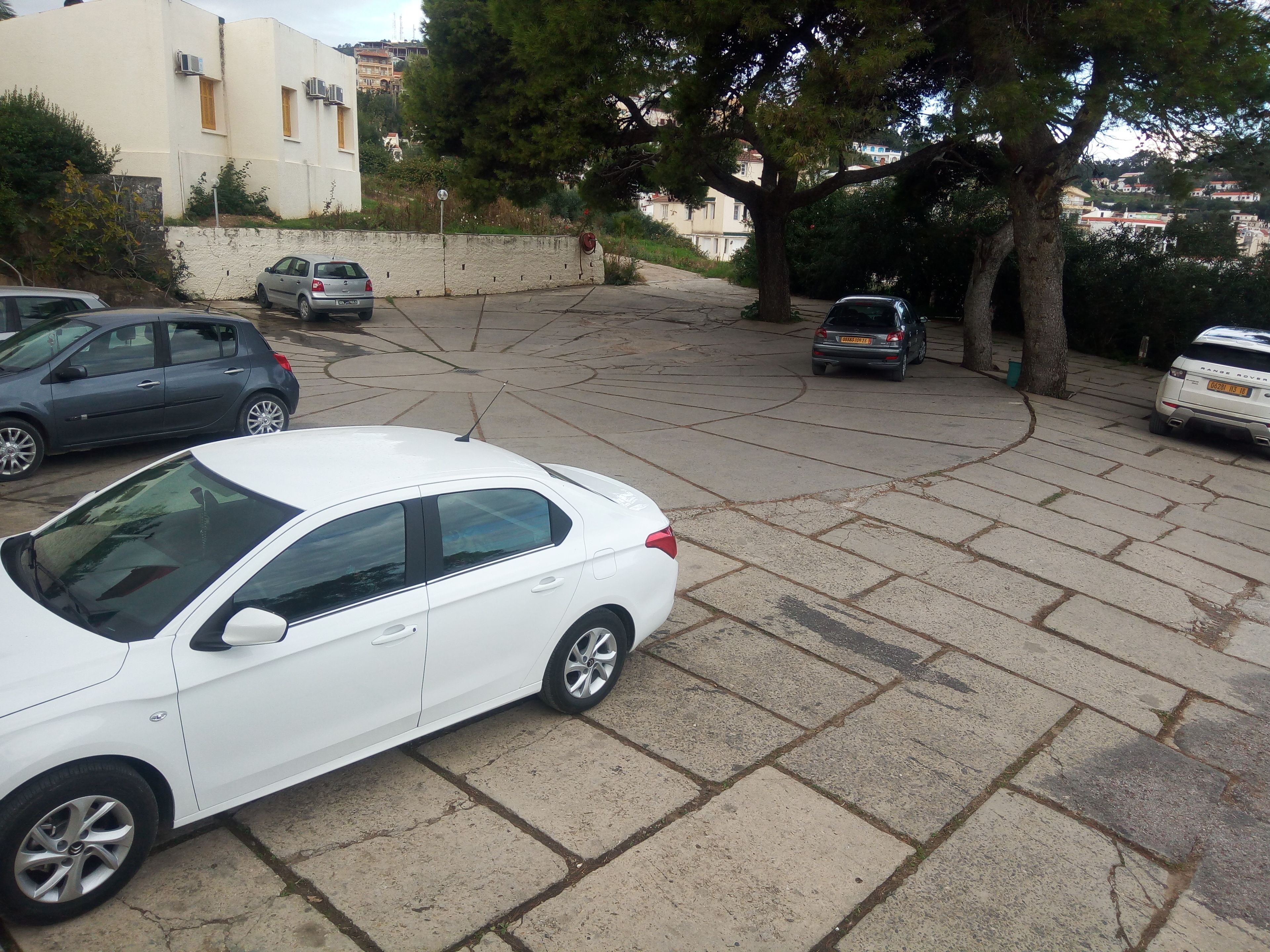 A parking area with several cars, including a white sedan and a Range Rover.