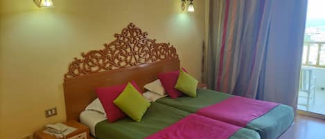 A double bed with a wooden headboard, two bedside tables with lamps, and a view of the outside through a balcony with curtains.