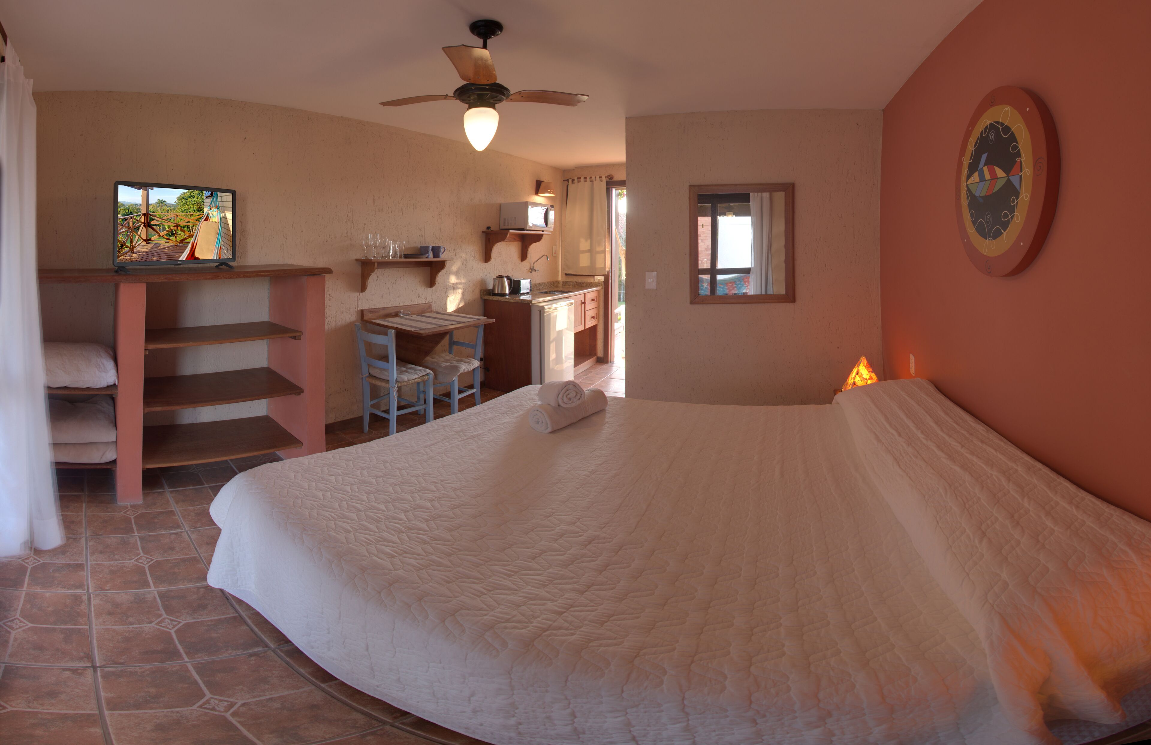 Un dormitorio con una cama grande, un escritorio y una silla. Hay un ventilador de techo, una ventana y un cuadro en la pared.