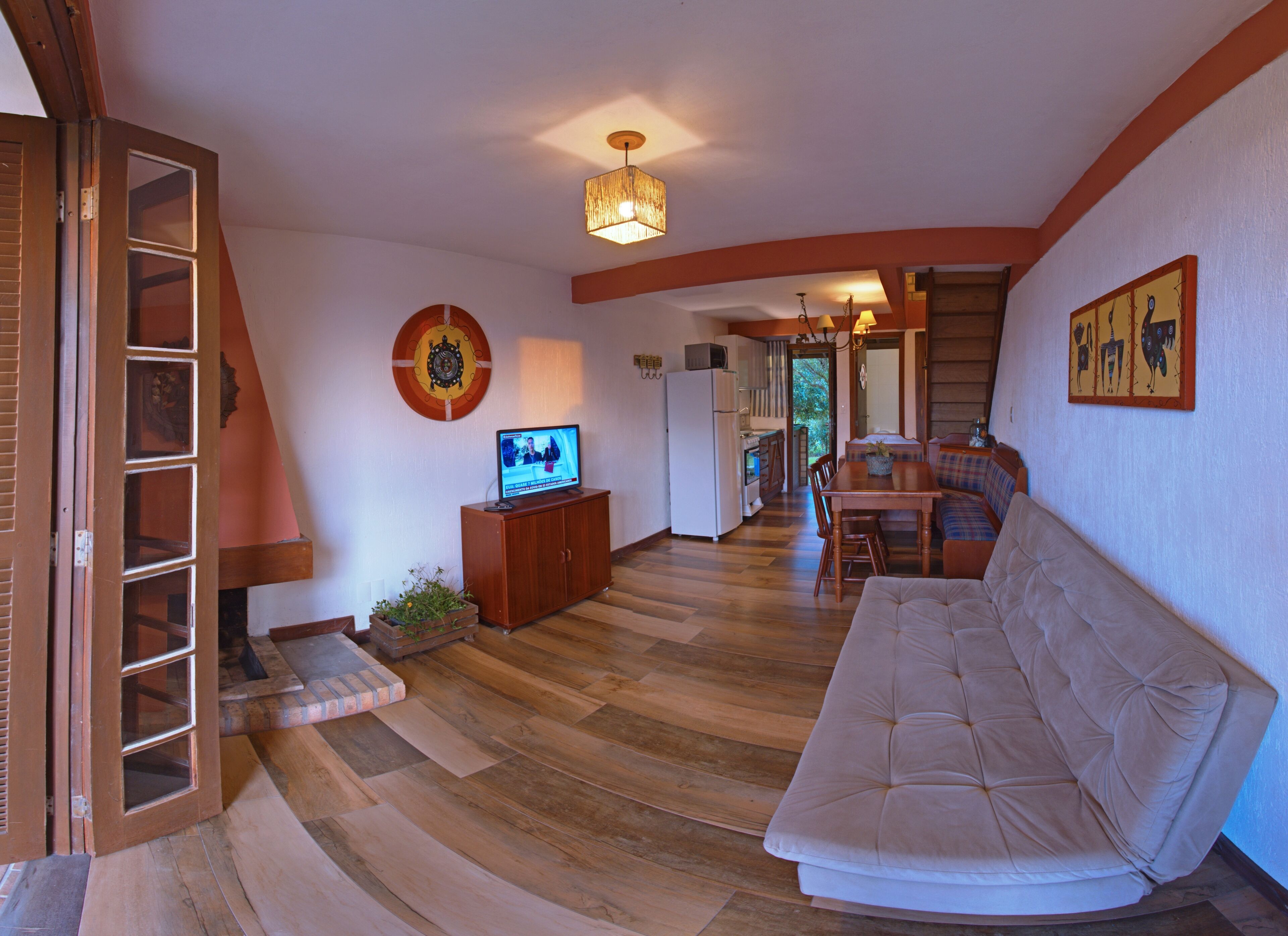 A spacious living room with a wooden floor, a beige sofa, a television, and a dining area with a wooden table and chairs.