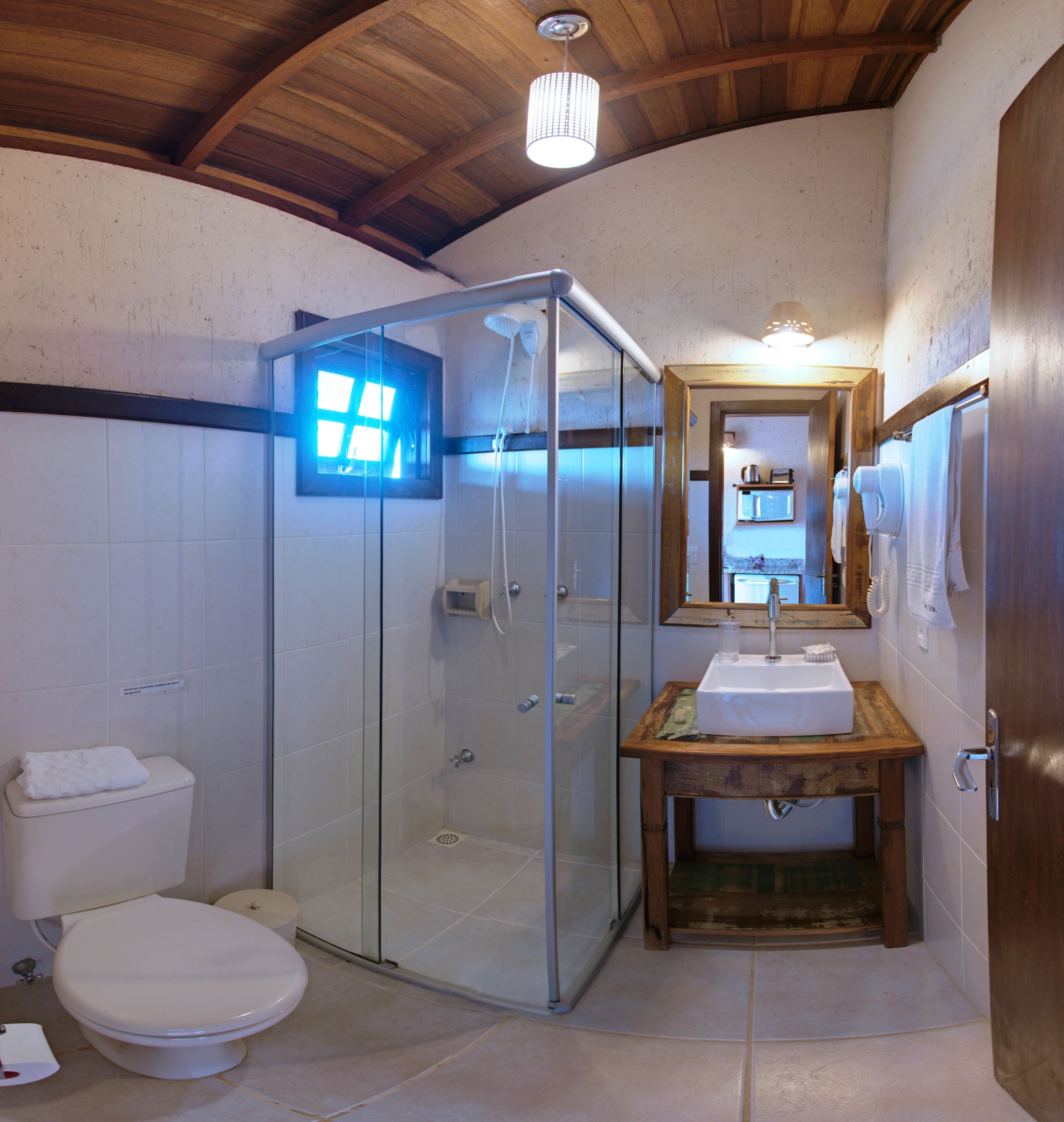Un baño con ducha de vidrio, inodoro, lavabo con encimera de madera y espejo sobre el lavabo.