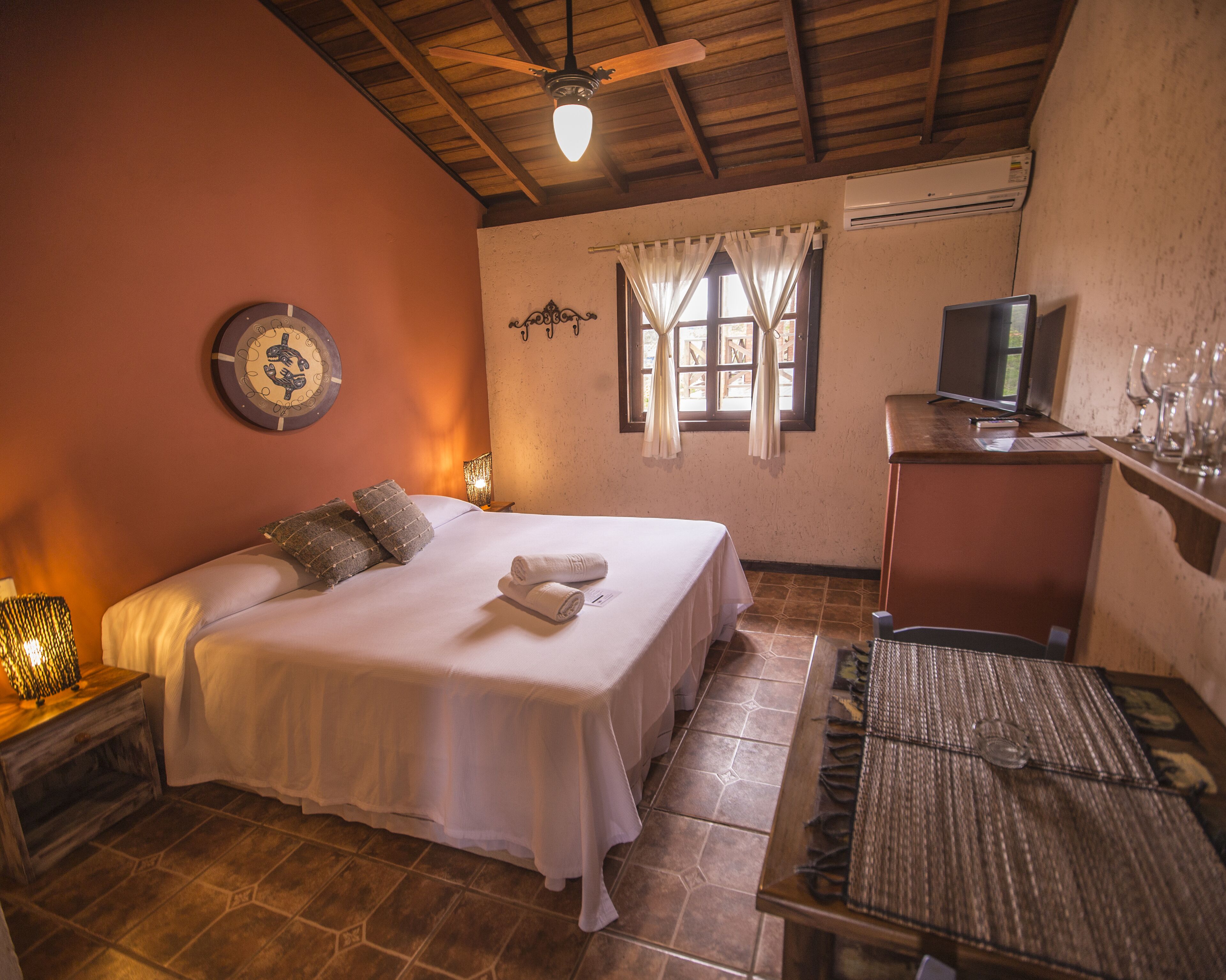 Una habitación con cama, escritorio, televisor y ventana con cortinas.