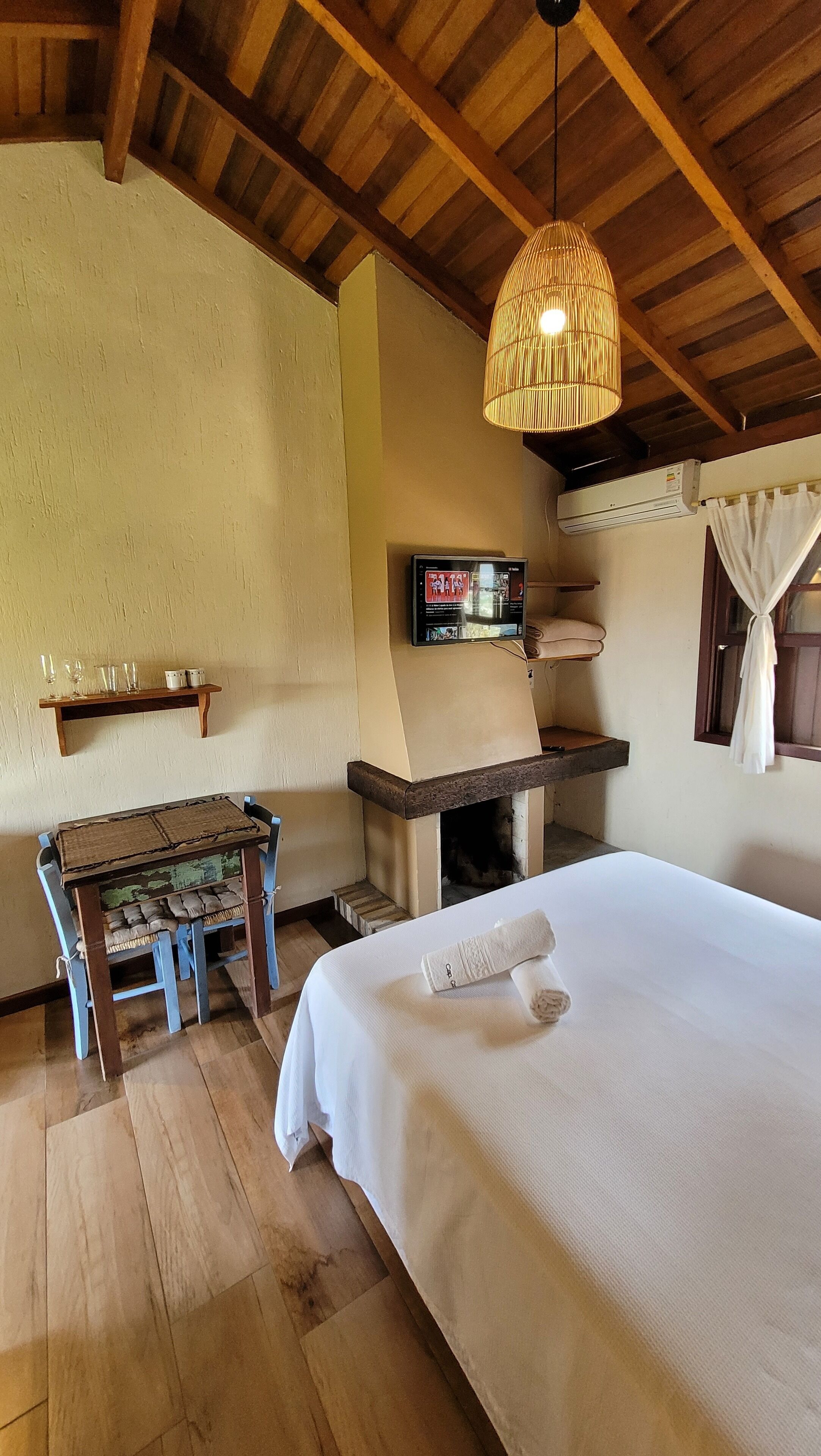 Una habitación acogedora con una cama, un banco de madera, una mesita pequeña, aire acondicionado instalado en la pared y una lámpara colgante.