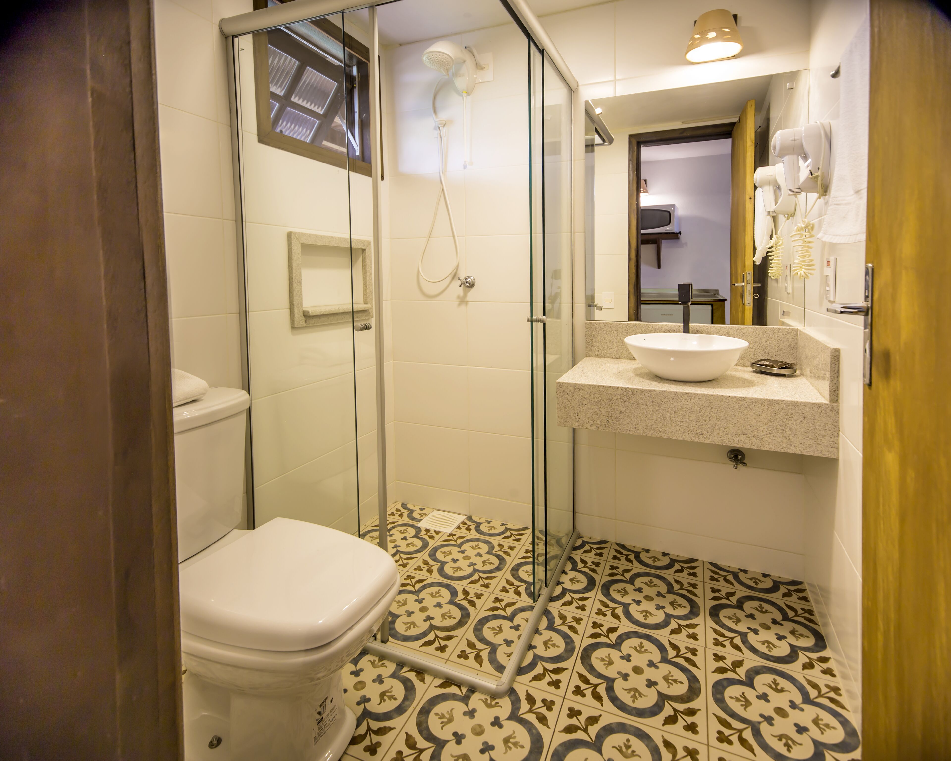 Un baño con ducha de vidrio, inodoro blanco, lavamanos y baldosas de suelo con diseño.