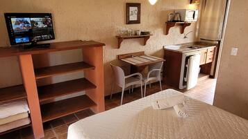 A compact room with a bed, a desk with a computer, a chair, a small kitchenette, and a ceiling fan.