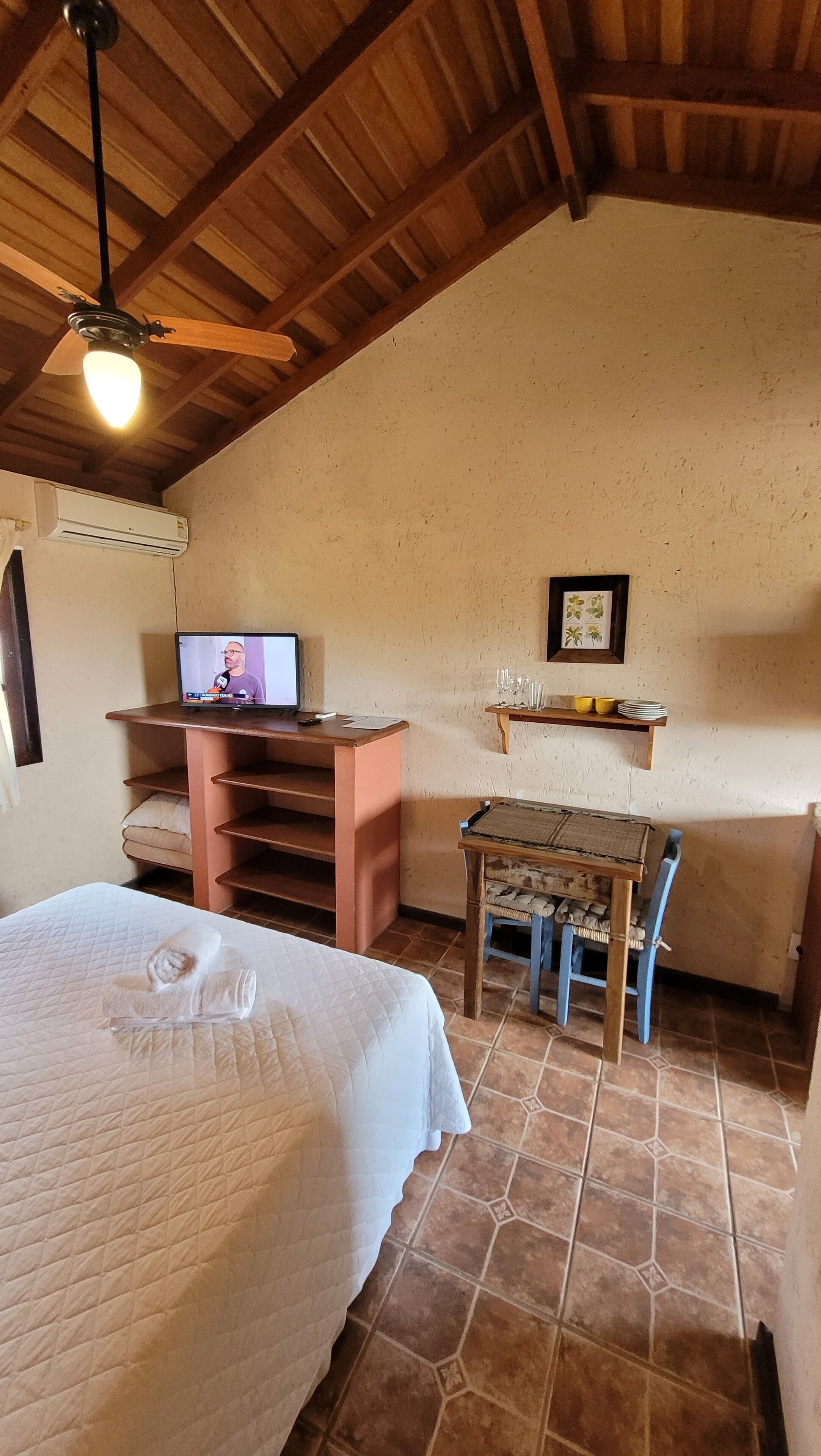 A cozy room with a bed, a desk with a computer, a chair, and a small table with glasses and plates.