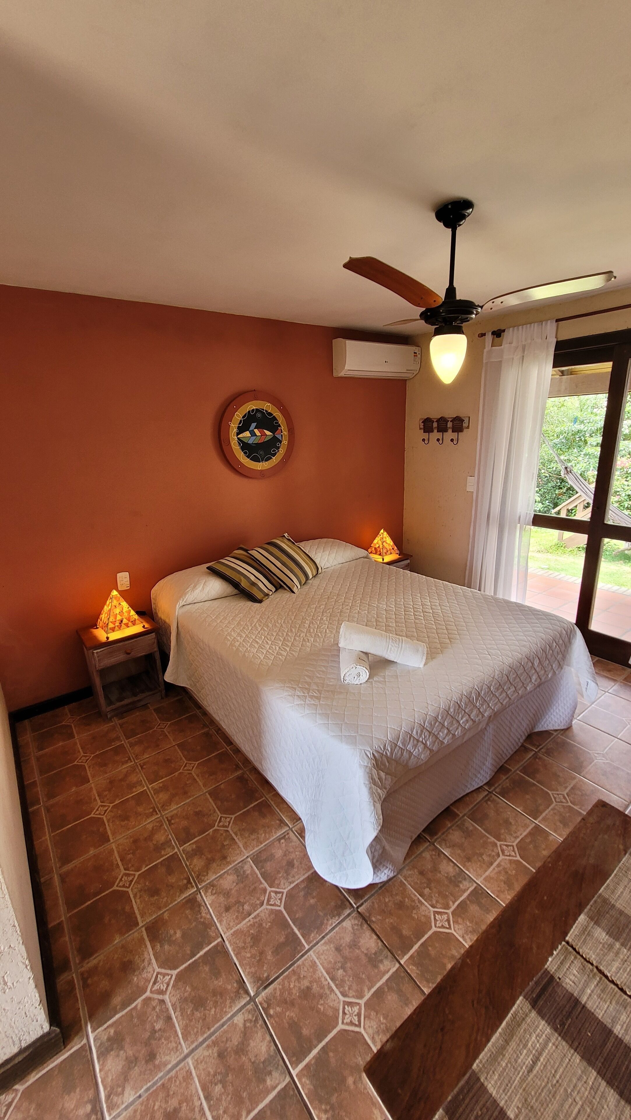 A bedroom with a bed, a nightstand, a ceiling fan, an air conditioning unit, and a view of the outdoors.