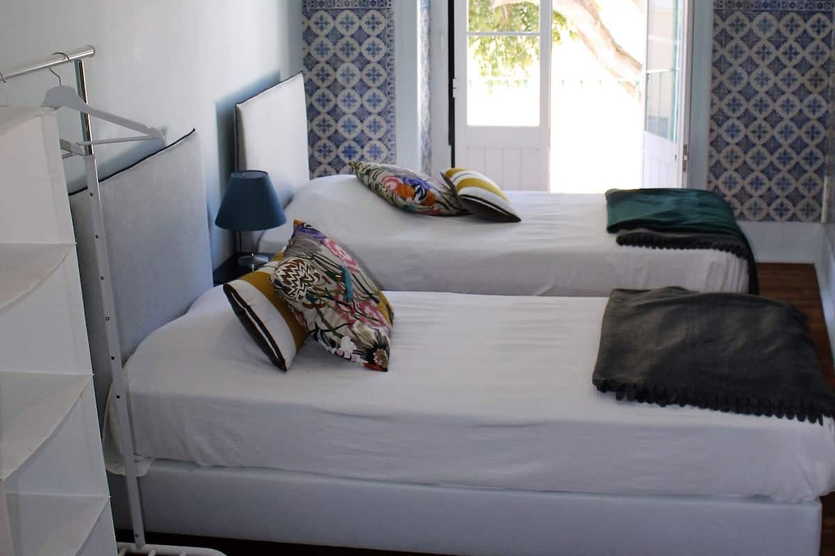 A hotel room with two beds, a wardrobe, a window with a view, and a door leading outside.