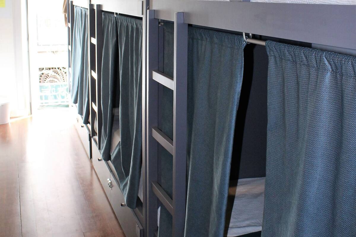 A row of bunk beds with curtains, a wooden floor, and a hanging light fixture.