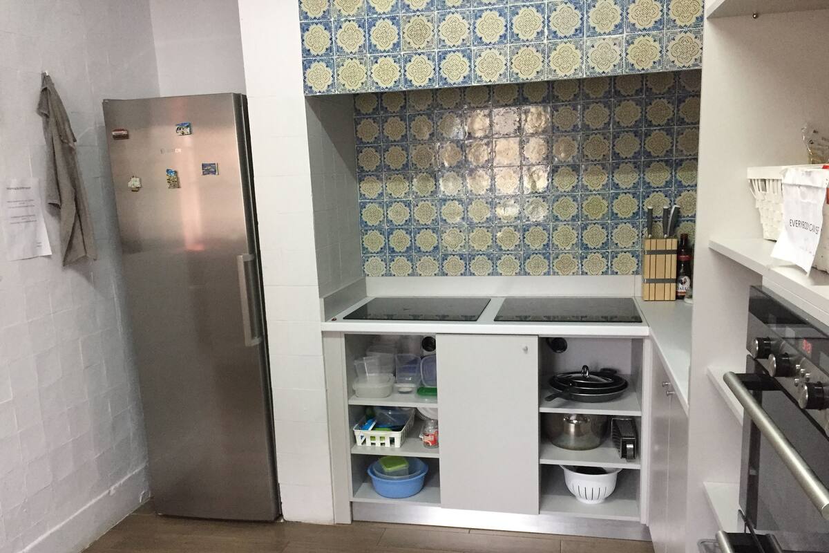 A compact kitchen with a stainless steel refrigerator, a white cabinet with storage containers, and a patterned backsplash.