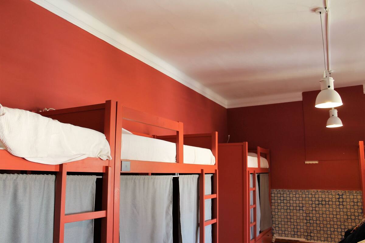 A dormitory room with bunk beds, a patterned wall, and a hanging light fixture.