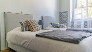 A bedroom with two beds, striped pillows, a grey blanket, and a blue lamp. - Back To Lisbon Hostel (Lisbon)