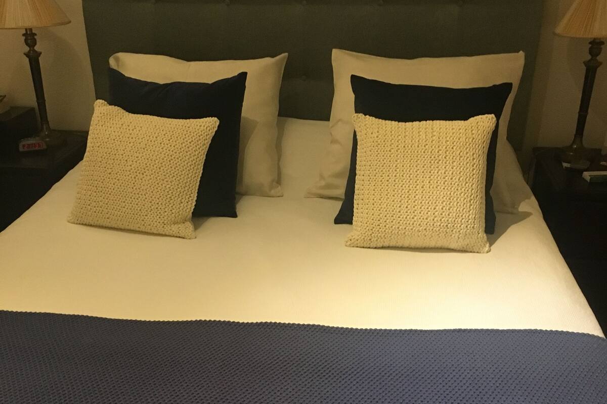 A neatly made bed with a dark headboard, two white pillows, and a blue bedspread.