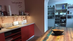 A kitchen with a wooden table, red cabinets, and a wall-mounted shelf with kitchen items. - Back To Lisbon Hostel (Lisbon)