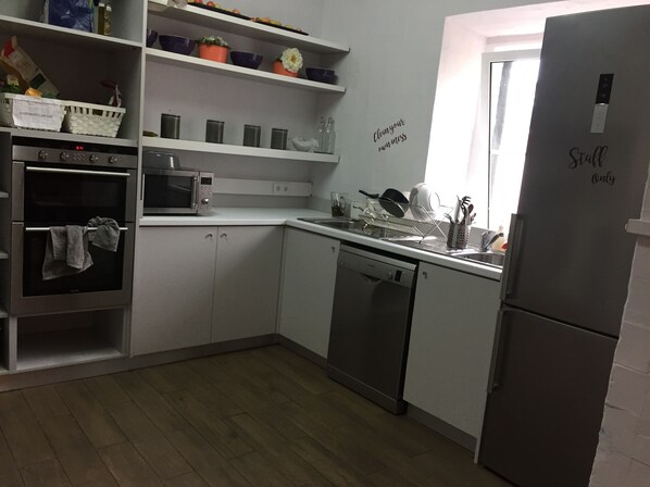 A kitchen with white cabinets, a stainless steel refrigerator, a dishwasher, a microwave, and a sink. - Back To Lisbon Hostel (Lisbon)