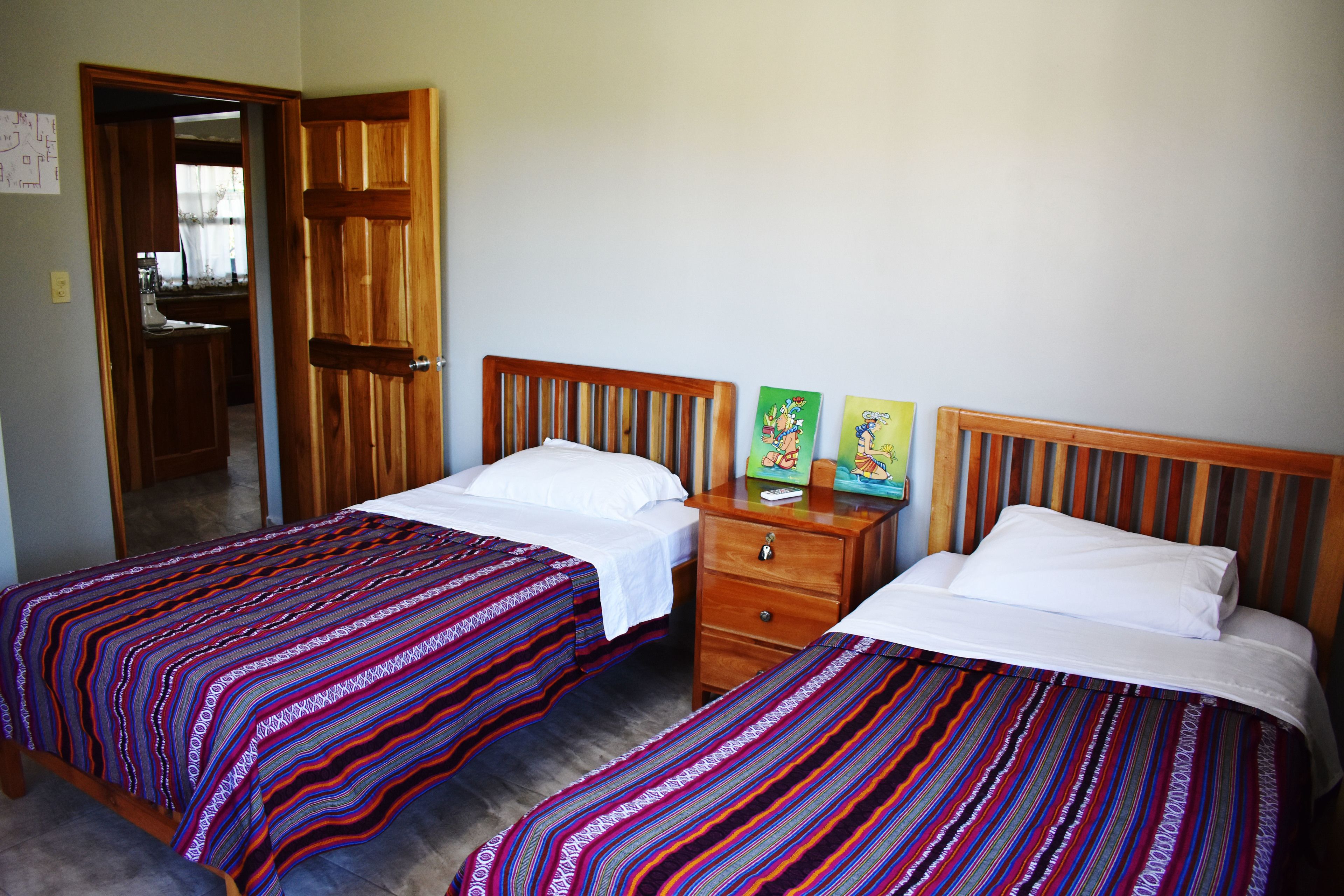 A room with two beds, each with a striped bedspread, a wooden headboard, and a nightstand with a drawer.