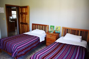 A room with two beds, each with a striped bedspread, a wooden headboard, and a nightstand with a drawer.