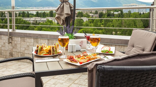 Een balkon met een gedekte tafel voor een maaltijd, met borden eten en bierglazen, met uitzicht op een bergachtig landschap.
