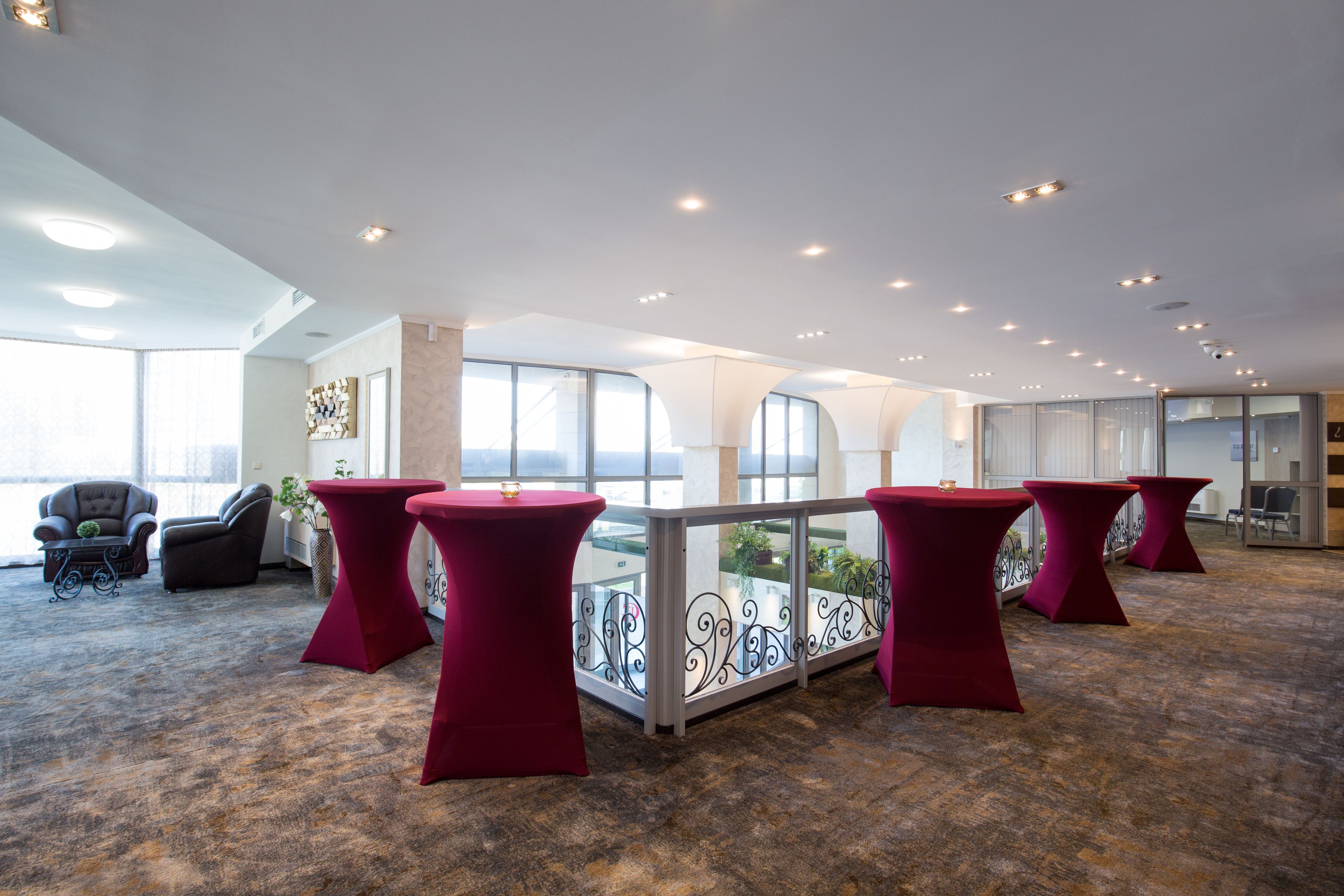 Una hall d'albergo moderna con tavoli rossi, una ringhiera in vetro e vista sulla città.