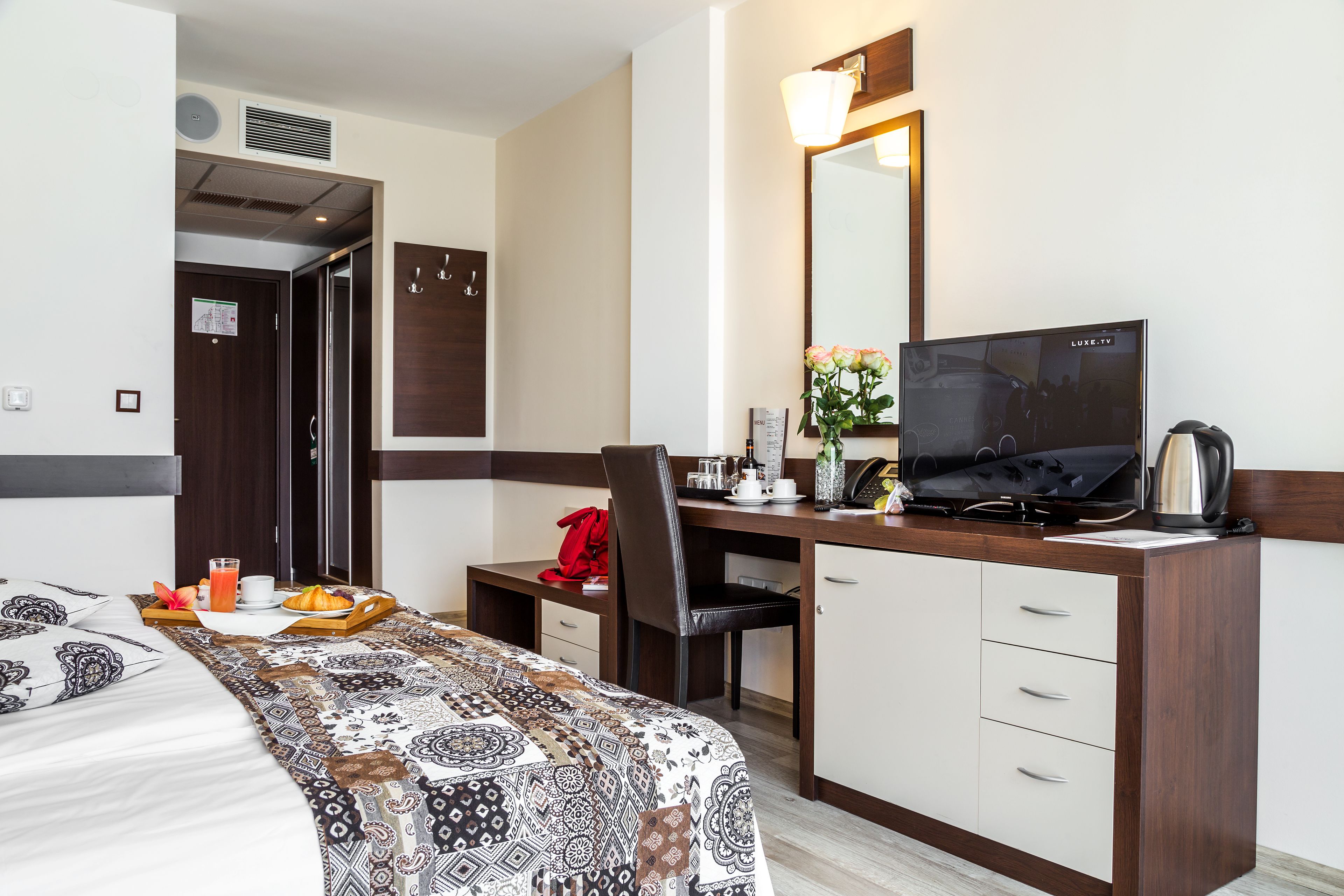 Una habitación de hotel con una cama, un escritorio con computadora, una silla, televisor y cafetera.