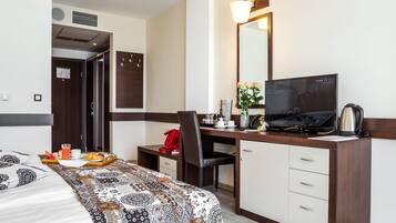 Una habitación de hotel con una cama, un escritorio con computadora, una silla, televisor y cafetera.
