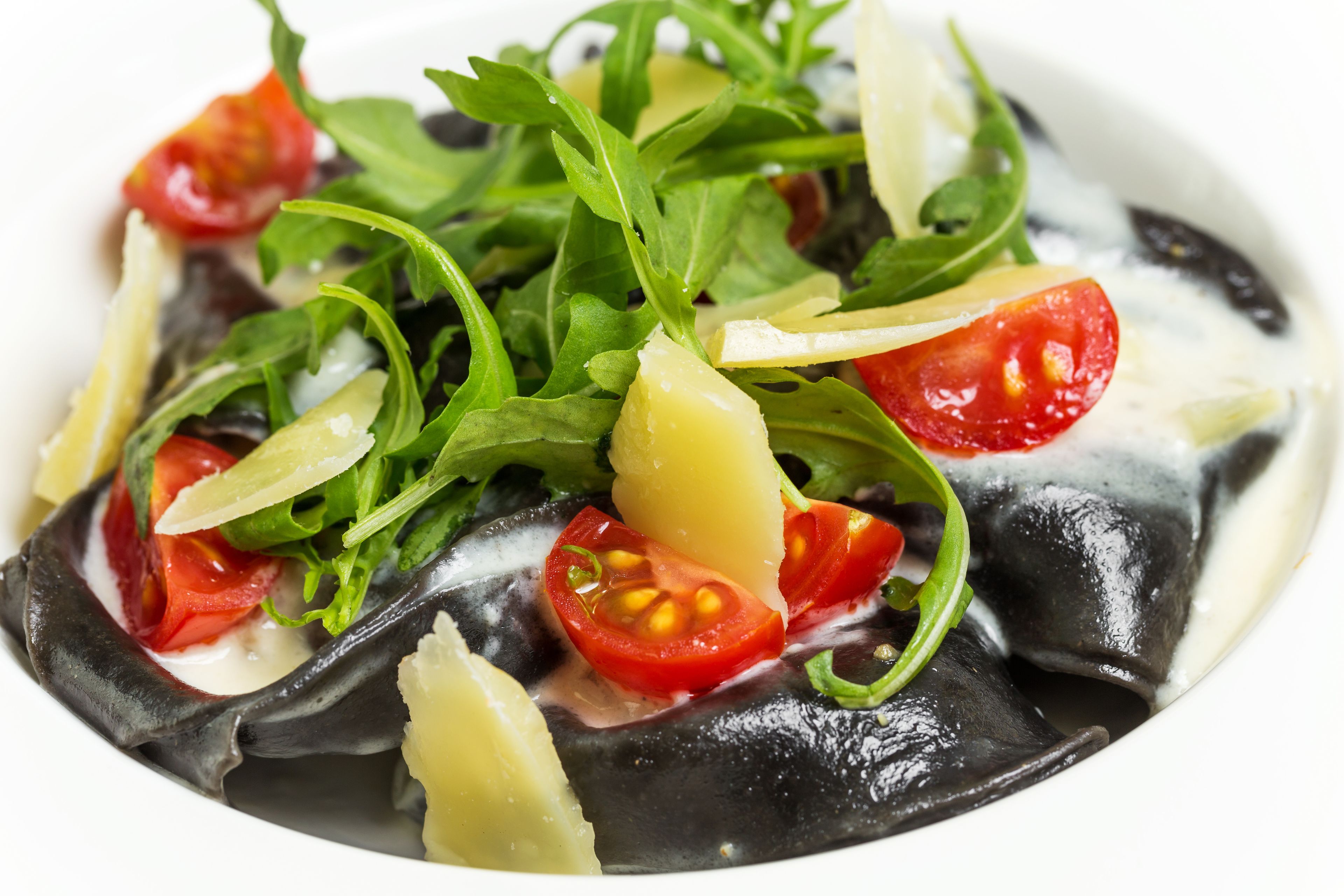 A dish with black fish, cherry tomatoes, and green leaves.