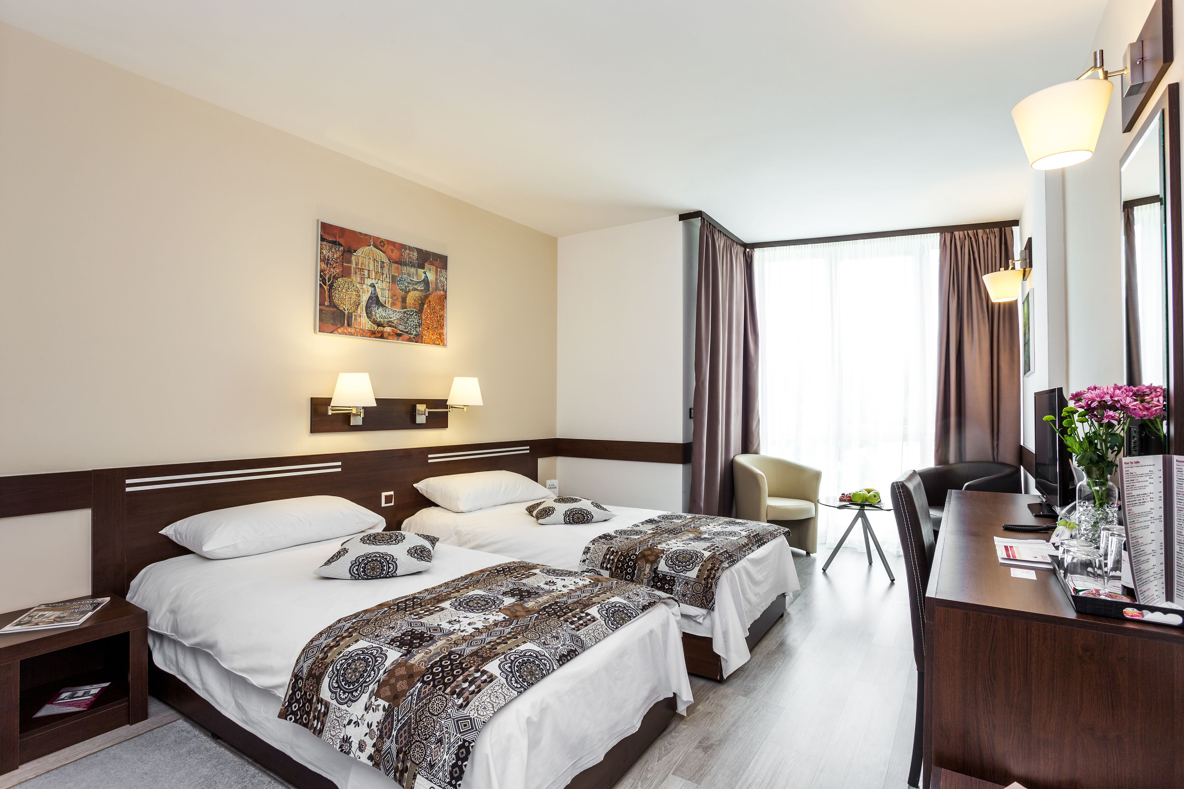 Une chambre d’hôtel avec deux lits, un bureau, une chaise, une petite table avec une plante et un tableau au mur.
