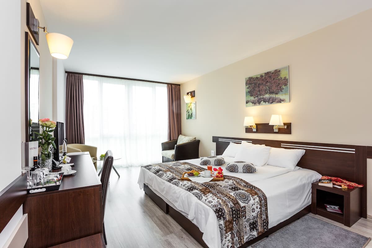 A hotel room with a large bed, a desk with a menu, a chair, a nightstand, and a painting on the wall.