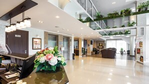 Een moderne hotel lobby met een receptiebalie, een grote bloemstuk en een trap naar een hoger gelegen niveau met groen.