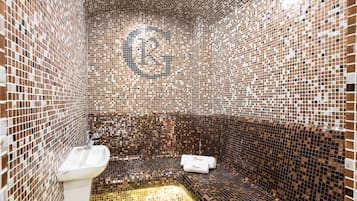 Bathroom features a mosaic tile design with a textured appearance, a pedestal sink, and a bench with a towel.