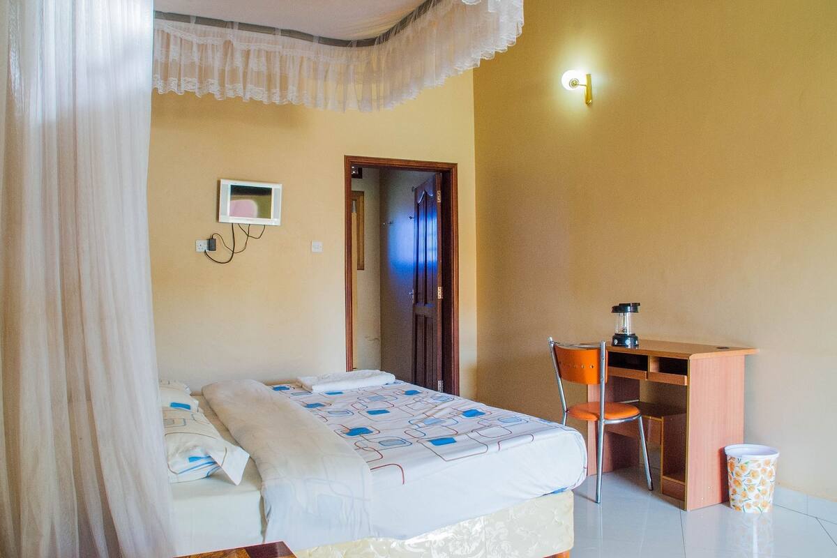 Makuuhuoneessa on sänky, työpöytä, tuoli ja pieni pöytä, jossa on lamppu.