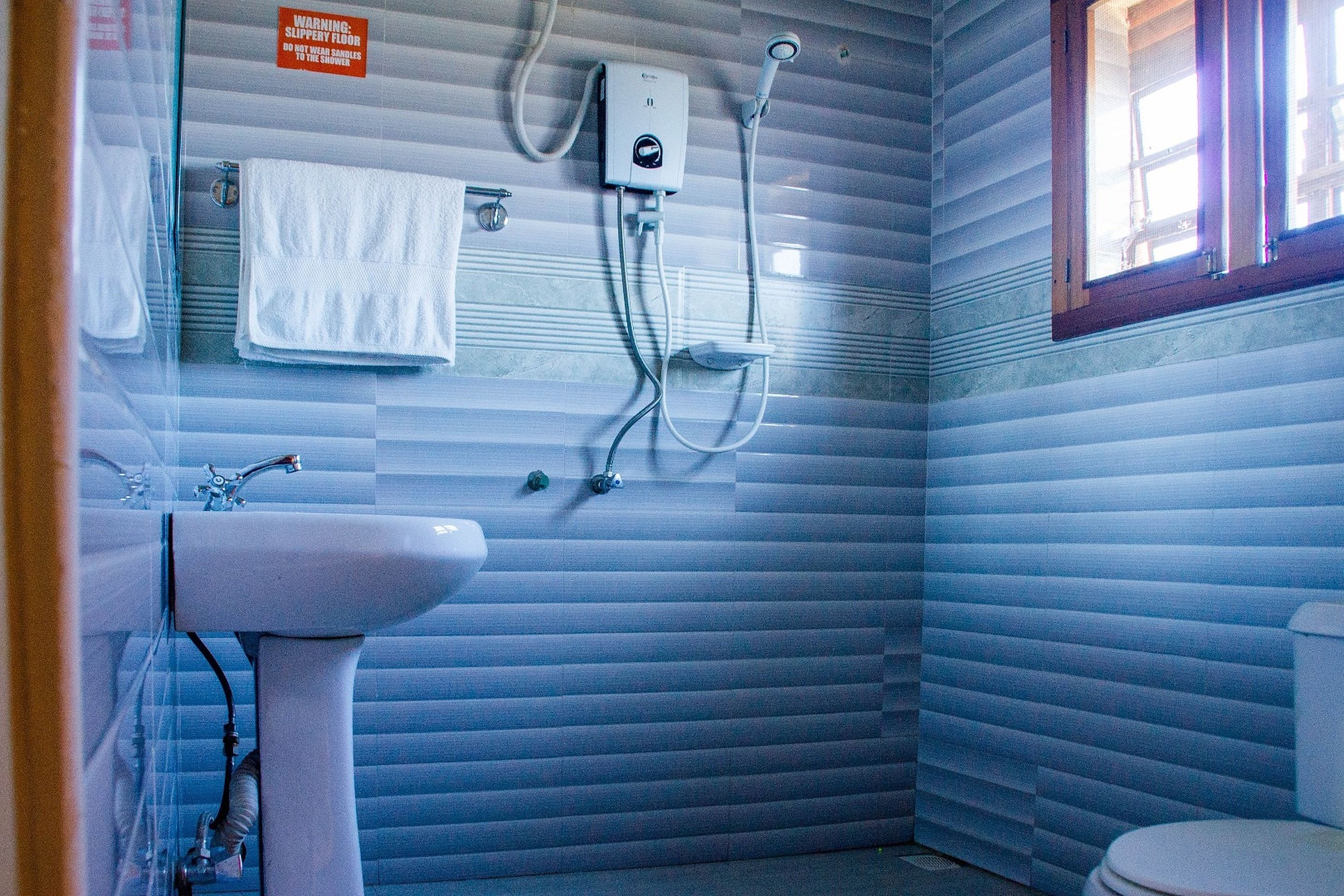 Een badkamer met een witte wastafel, een handdoekhouder, een douche en een toilet.