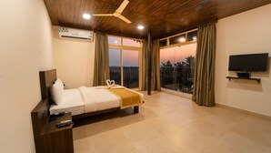 A bedroom with a bed, a TV, a ceiling fan, and a view through the window. - Kay's Riverview Resort (Arpora)