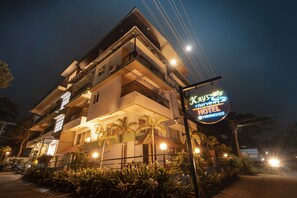 Um hotel com vários andares, varandas, uma entrada bem iluminada e uma placa.