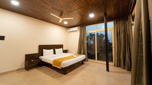 A modern hotel room with a wooden ceiling, a large bed with white linens, a nightstand, and a window with curtains. - Kay's Riverview Resort (Arpora)