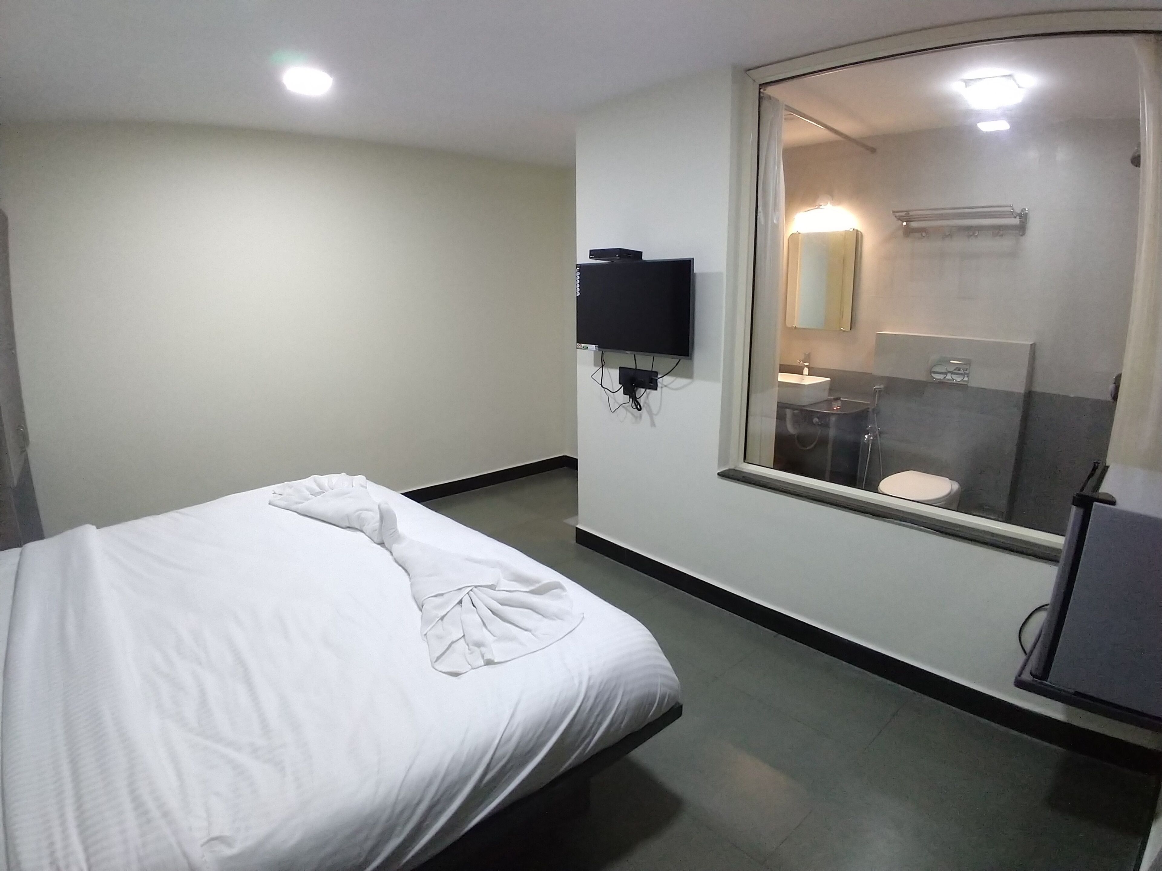 A hotel room with a bed, a TV mounted on the wall, and a bathroom visible through a glass door.