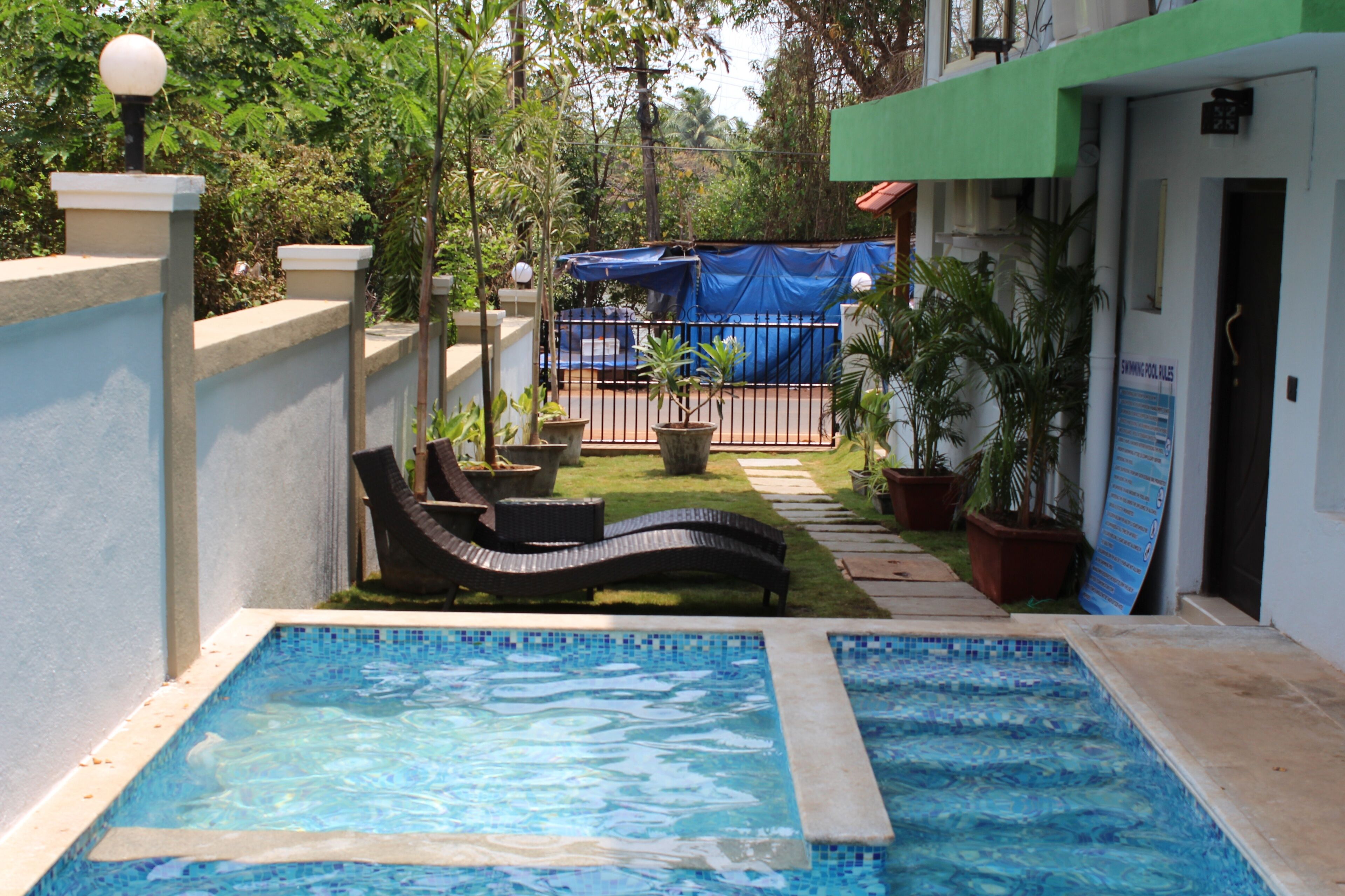 A swimming pool with lounge chairs, surrounded by potted plants and a covered area.