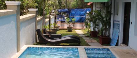 Una piscina con sillas de descanso, rodeada de plantas en macetas y una zona cubierta.