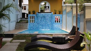 A swimming pool with a blue mosaic wall, a small waterfall feature, and wicker lounge chairs. - Kay's Riverview Resort (Arpora)