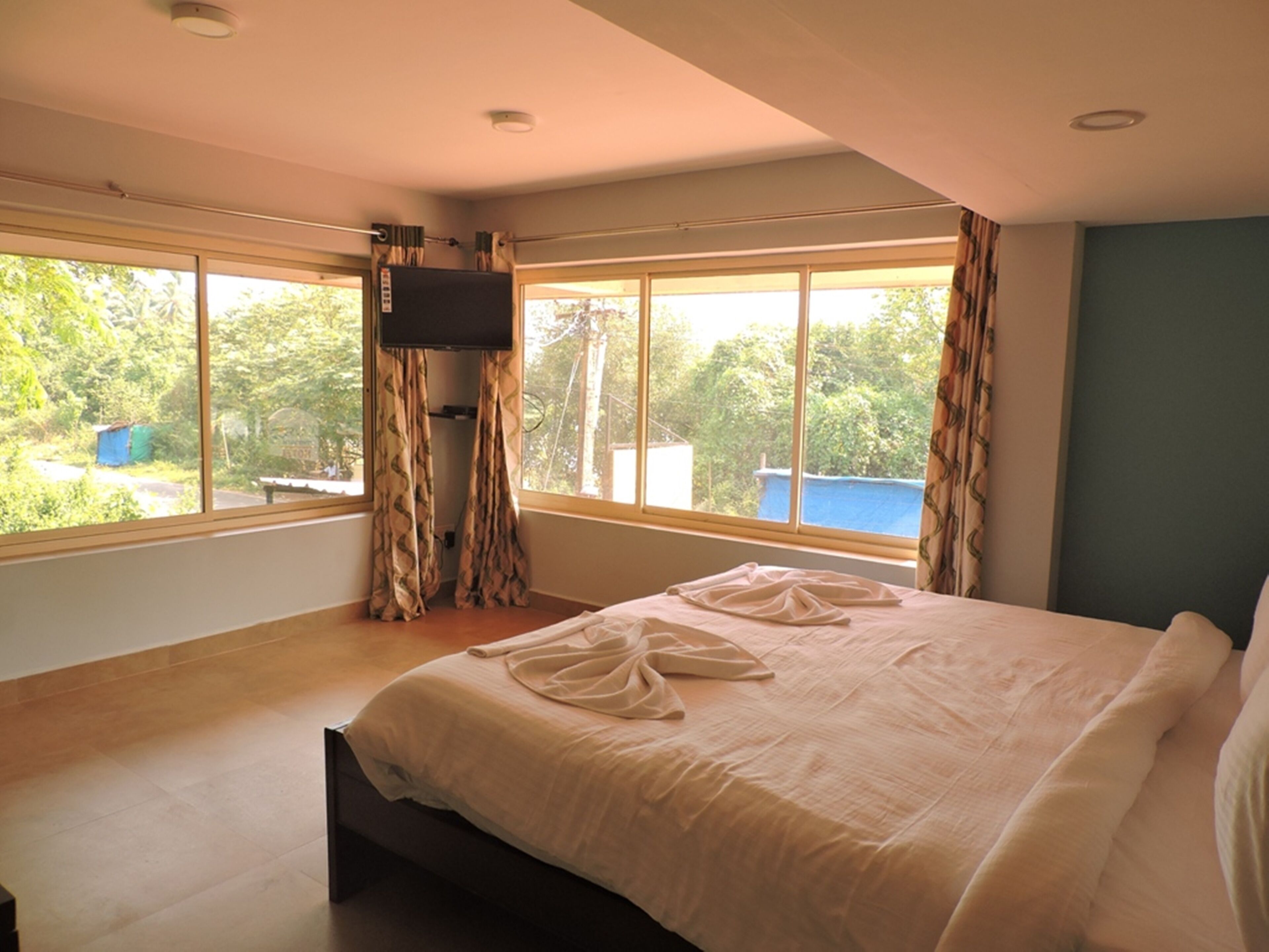 A bedroom with a large bed, a TV mounted on the wall, and a window with curtains.