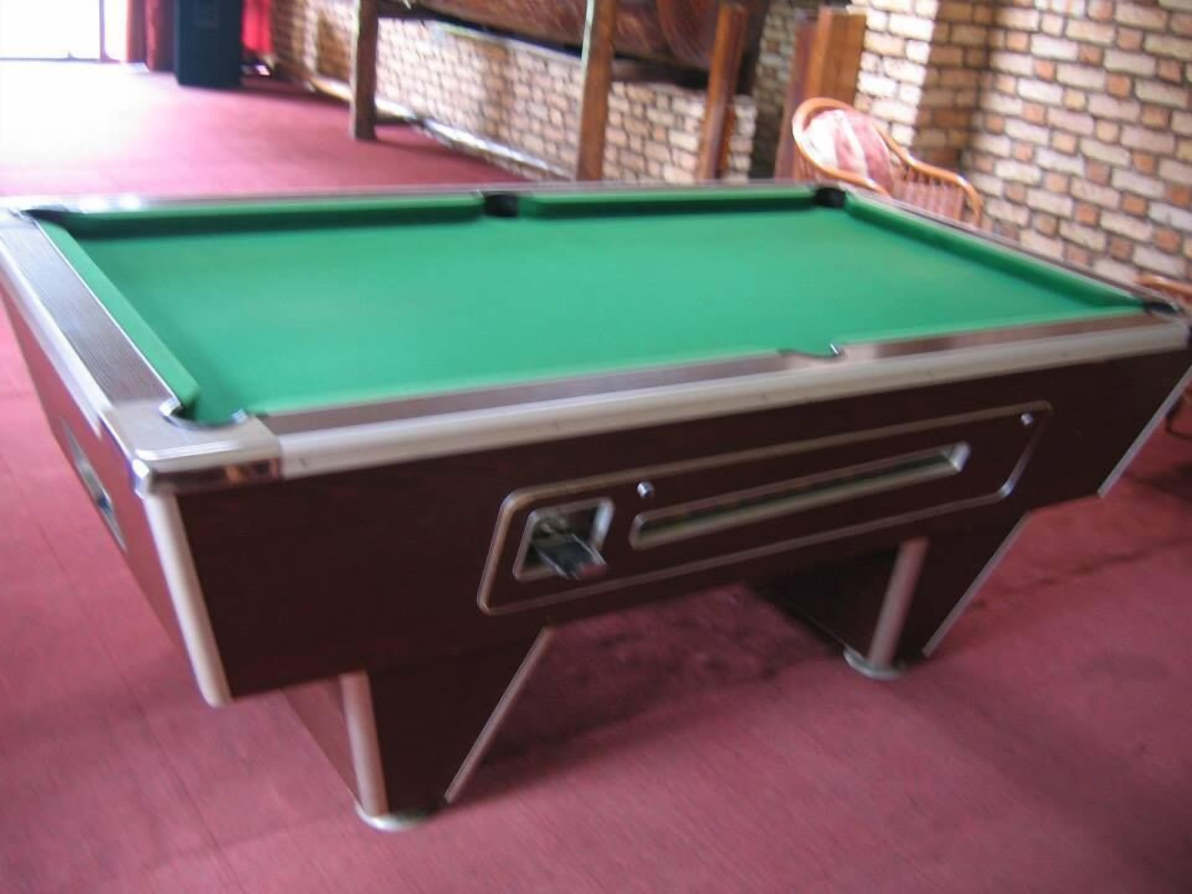 Una mesa de billar con superficie de fieltro verde, un cajón con asa y un suelo cubierto de alfombra roja.