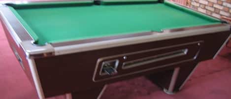 Una mesa de billar con superficie de fieltro verde, un cajón con asa y un suelo cubierto de alfombra roja.
